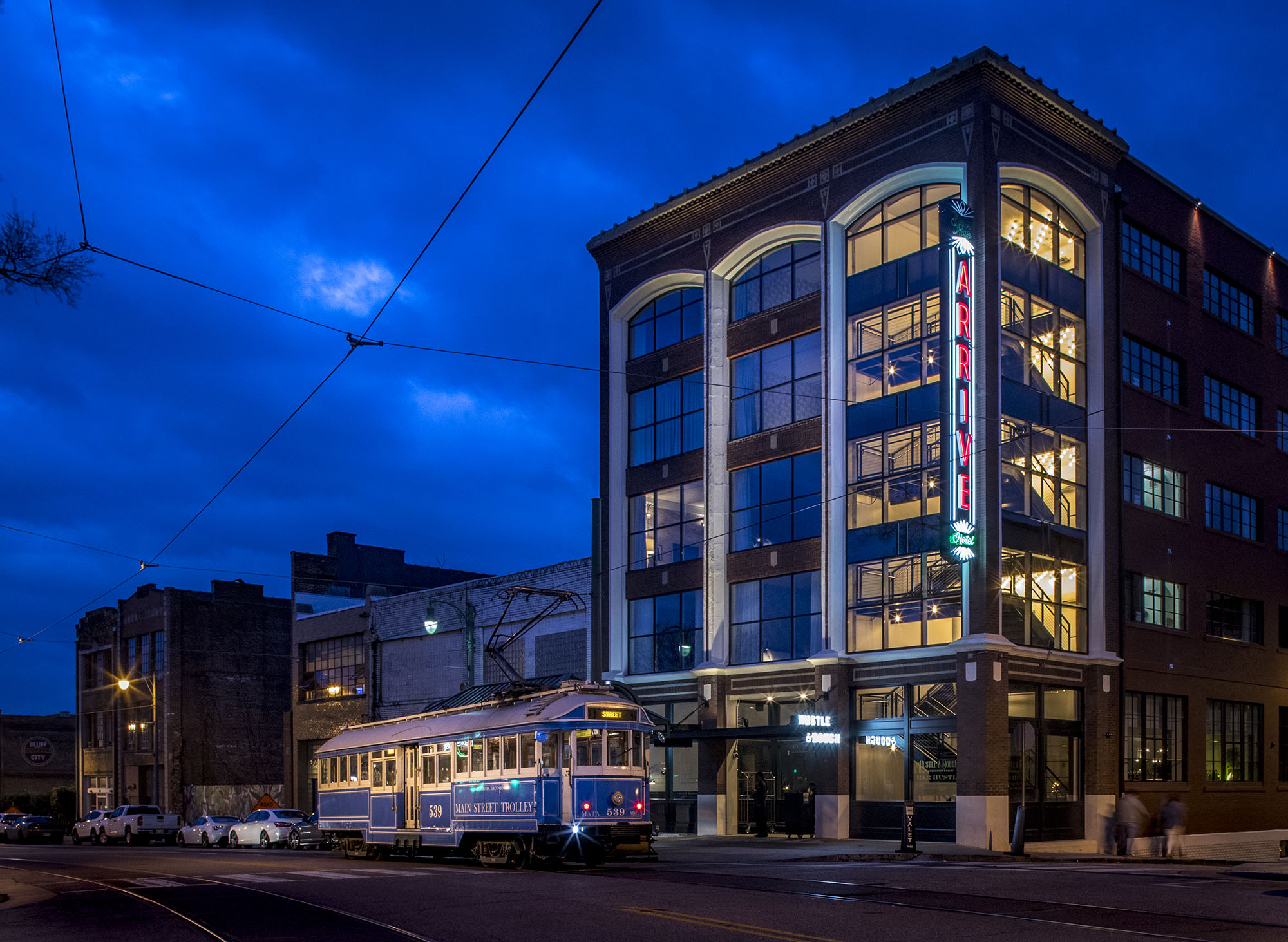 ARRIVE Memphis at night with it's neon sign illuminated and a trolley out front on South Main Street. 