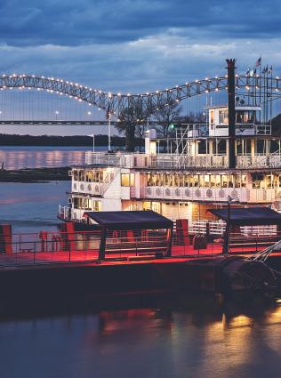 Riverboat on the Mississippi River at dusk with the Hernando de Soto Bridge in the background.