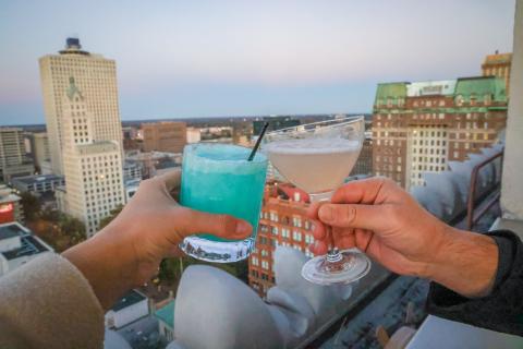 two cocktails cheersing overlooking city skyline from hu rooftop