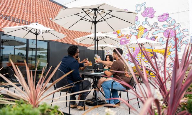 Four friends sitting on the outdoor patio toasting drinks at JEM.