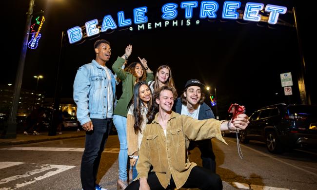 Friends pose for photo beneath the neon Beale Street sign.
