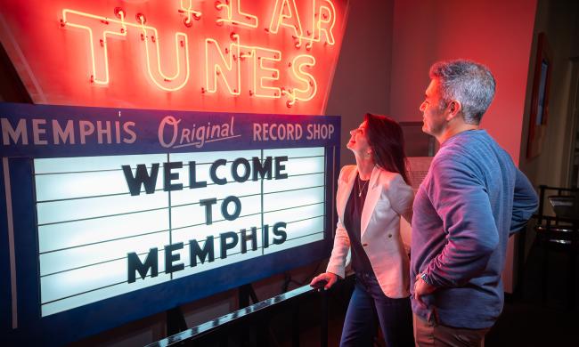 Couple touring Rock 'n' Soul Museum, looking at a "Welcome to Memphis" popular tunes neon sign.