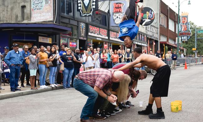 Beale Street Flippers flip over crouched group on Beale Street with a crowd watching.