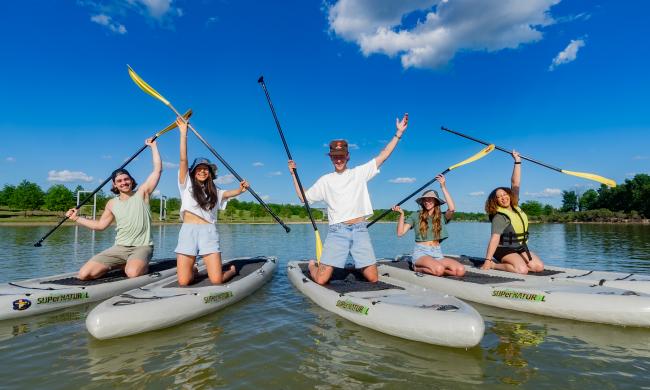 Group of paddle boarders pose for photo holding up oars on boards at Shelby Farms Park.