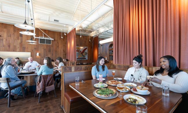 People dining at Hog and Hominy at a table full of pizzas and apps.