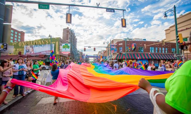 People marching in the annual Pride Parade, stretching a rainbow flag over Beale Street.