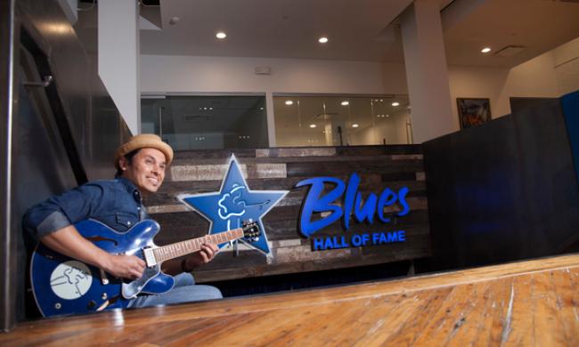A man playing a blue guitar at the Blues Foundation's Blues Hall of Fame.
