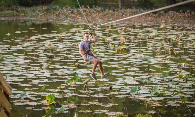 A man zip lining across a body of water filled with lily pads on Shelby Farms' Go Ape zip line course.
