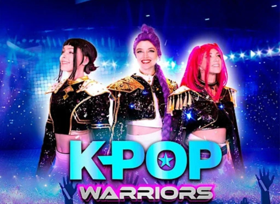 KPOP Warriors promotional artwork featuring three costumed performers with colorful hair on a bright blue stage, with the KPOP Warriors logo displayed prominently in front.