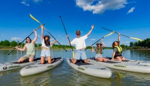 Group of paddle boarders pose for photo holding up oars on boards at Shelby Farms Park.