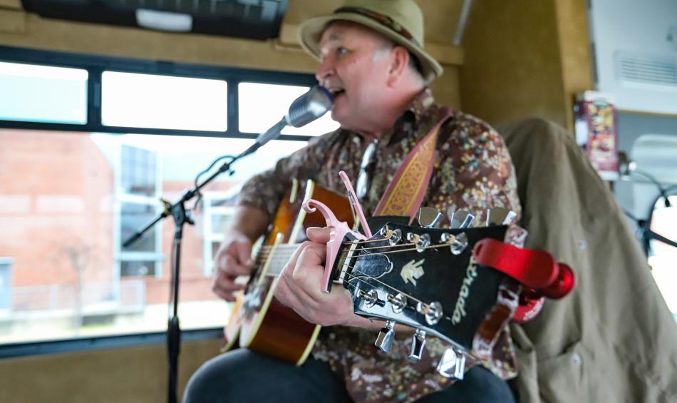 A tour guide and musician sings to patrons on a Backbeat Tour. They are dressed in a fedora and are strumming a guitar as they sing into a microphone.