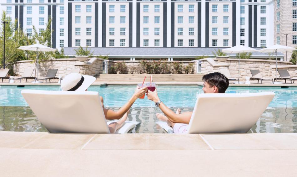 Couple tapping drink glasses together while lounging at the pool at Guesthouse at Graceland.